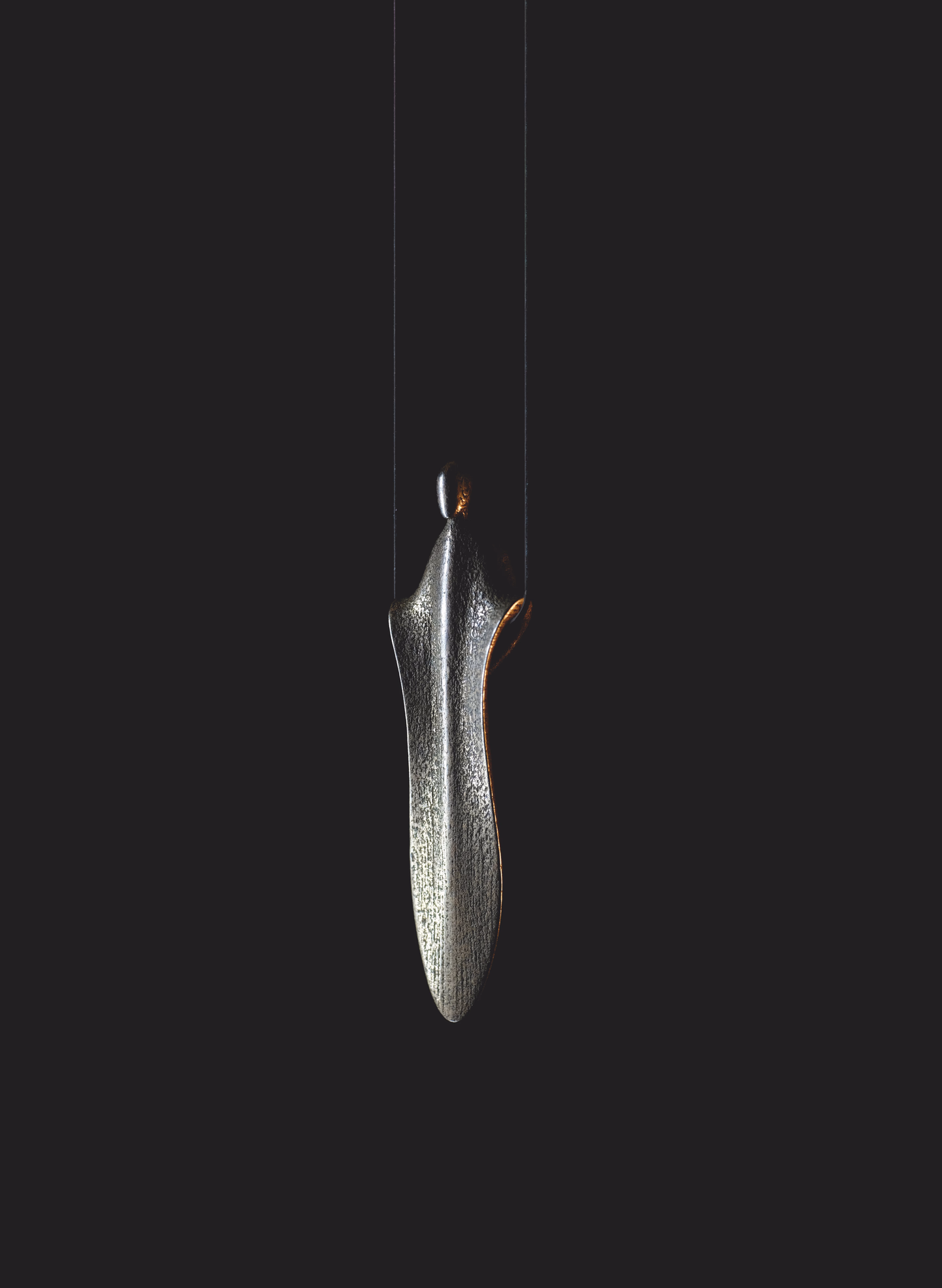 Presence in silver, hanging on a fine cord against a dark ground